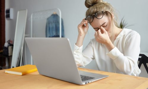 Modern technology, job and people concept. Portrait of tired young female employee with hair bun taking off eyeglasses and massaging her nose bridge, feeling stressed because of lot of work